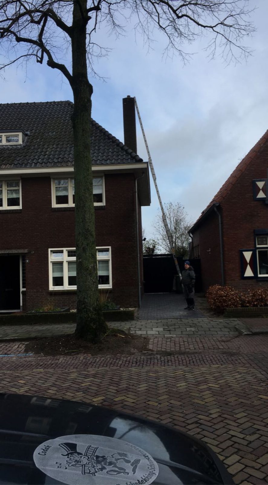 Ladder tegen de schoorsteen van een bakstenen woning, met de Co-Dak sticker op de motorkap op de voorgrond